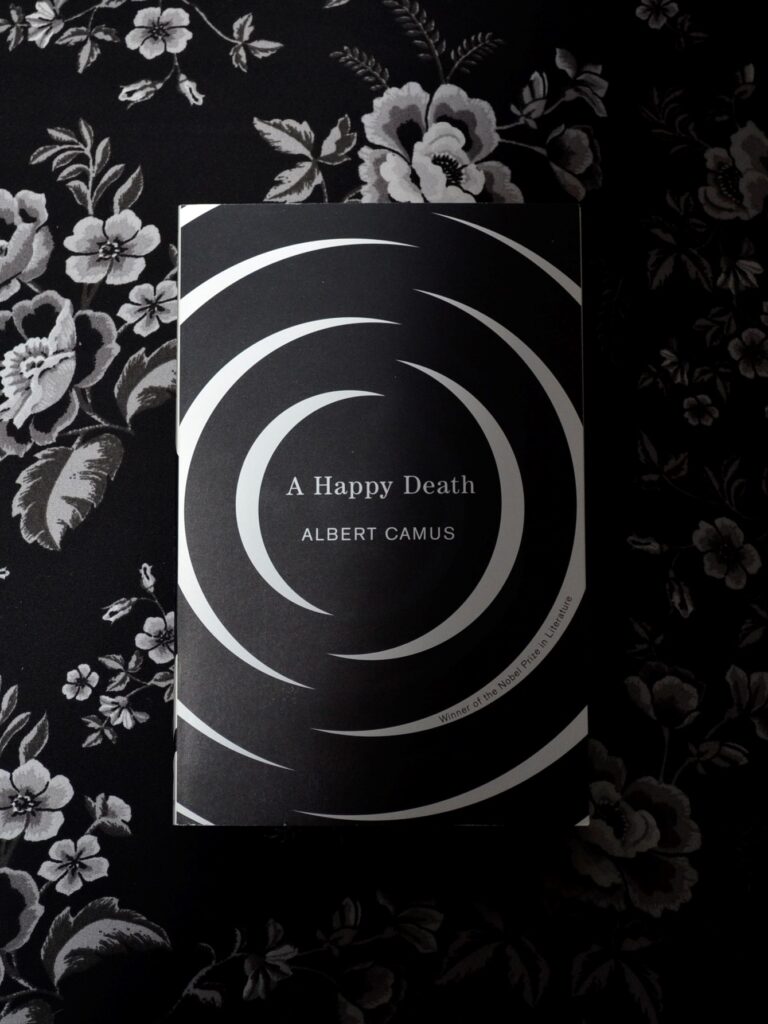 The black and white cover of A Happy Death on a black and white floral background in shadow.