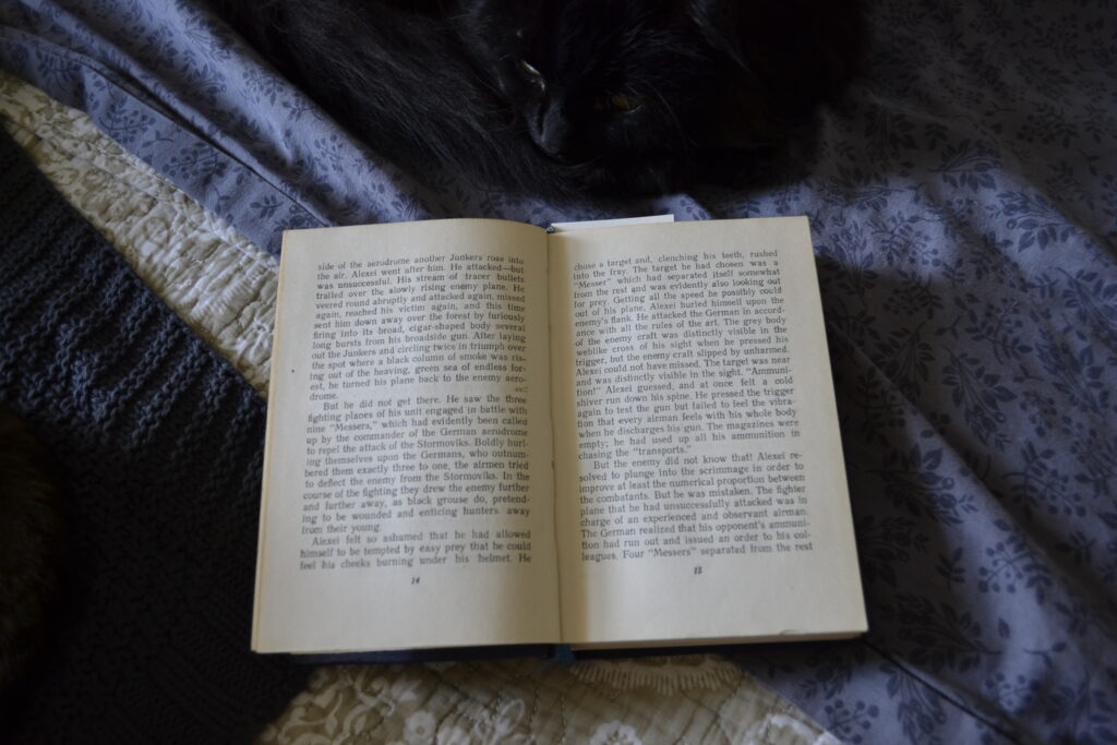 A black cat sleeps beside the open pages of Polevoy's A Story of a Real Man.