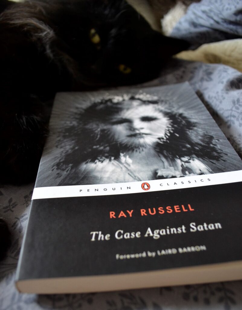 A black cat peers over The Case Against Satan.