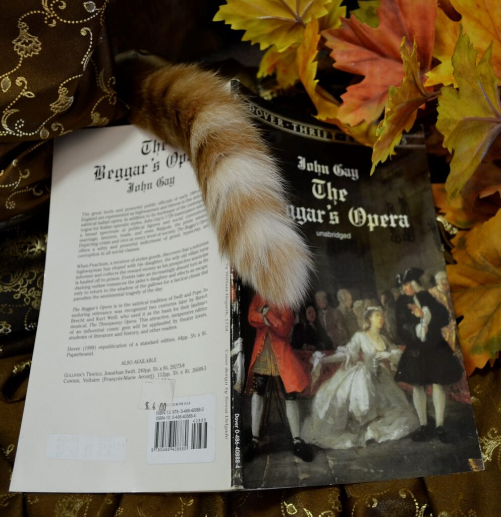 An orange tabby's tail rests along the spine of The Beggar's Opera.