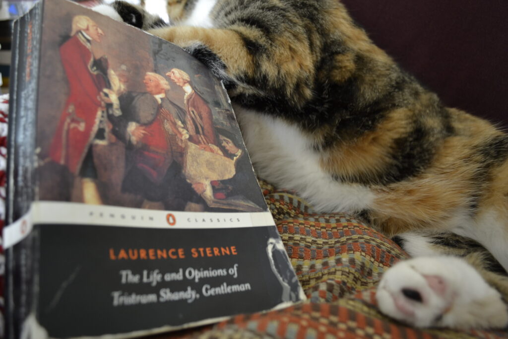 A calico tabby leans near a copy of Tristram Shandy.