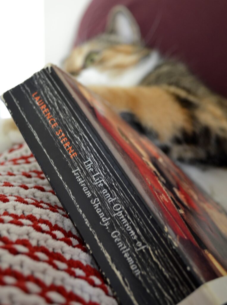 A calico tabby cat languishes behind a beaten copy of Tristram Shandy.