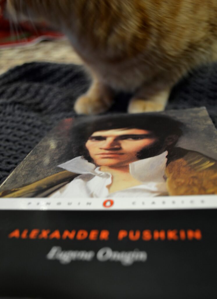 An orange tabby cat crouches beside a copy of Eugne Onegin.