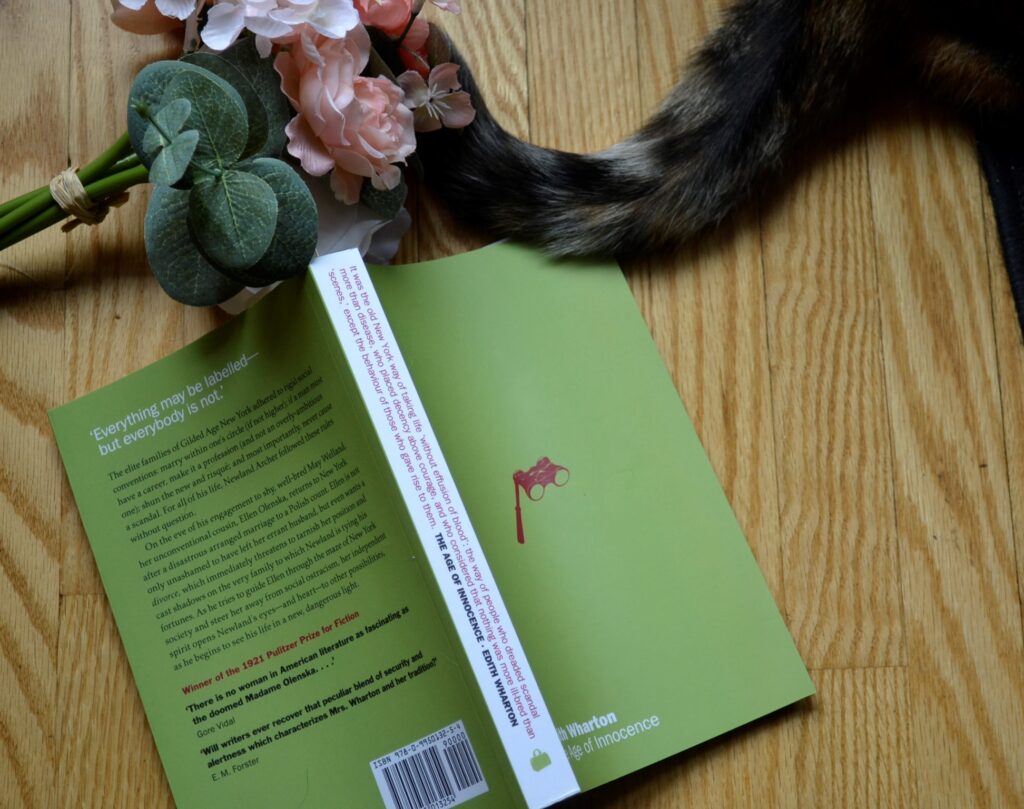 A calico cat tail and pink flowers beside a green book.