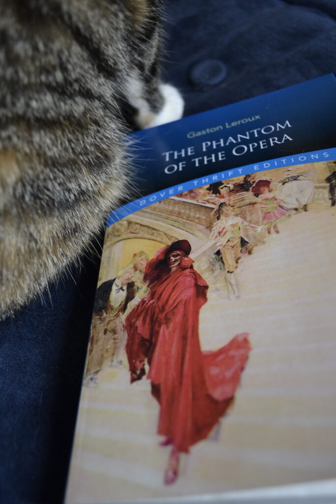 Calico paws beside The Phantom of the Opera.