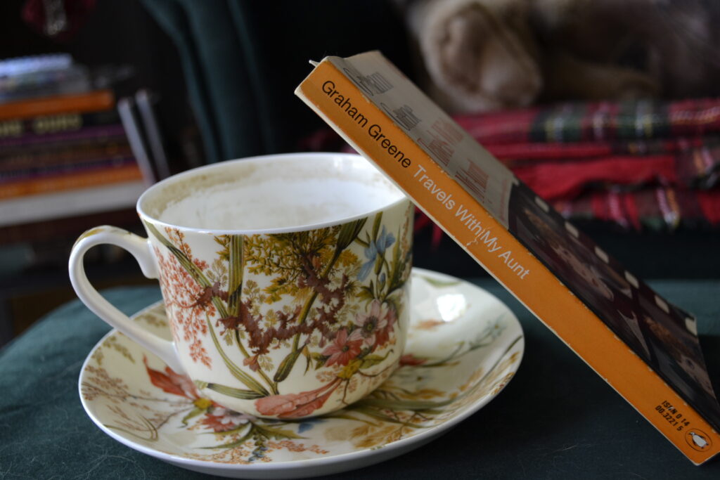 The orange wpin of Travels with My Aunt leans against a teacup.