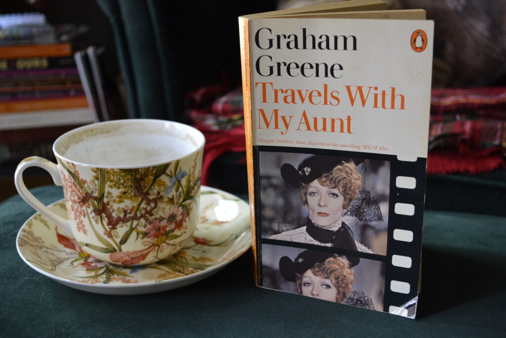 A teacup and the front cover of a vintage penguin edition of Travels with My Aunt.