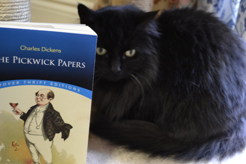 A black cat sits beside a copy of The PIckwick Papers.