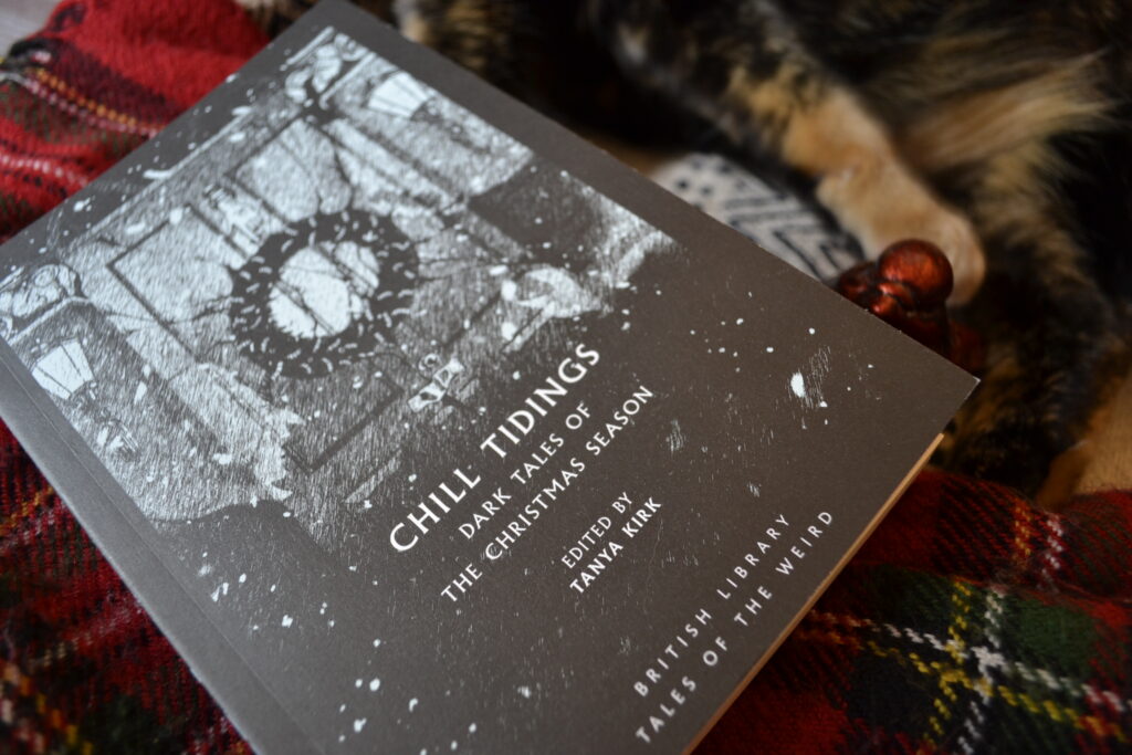 A closeup of the black and white cover of Chill Tidings and a red paw.