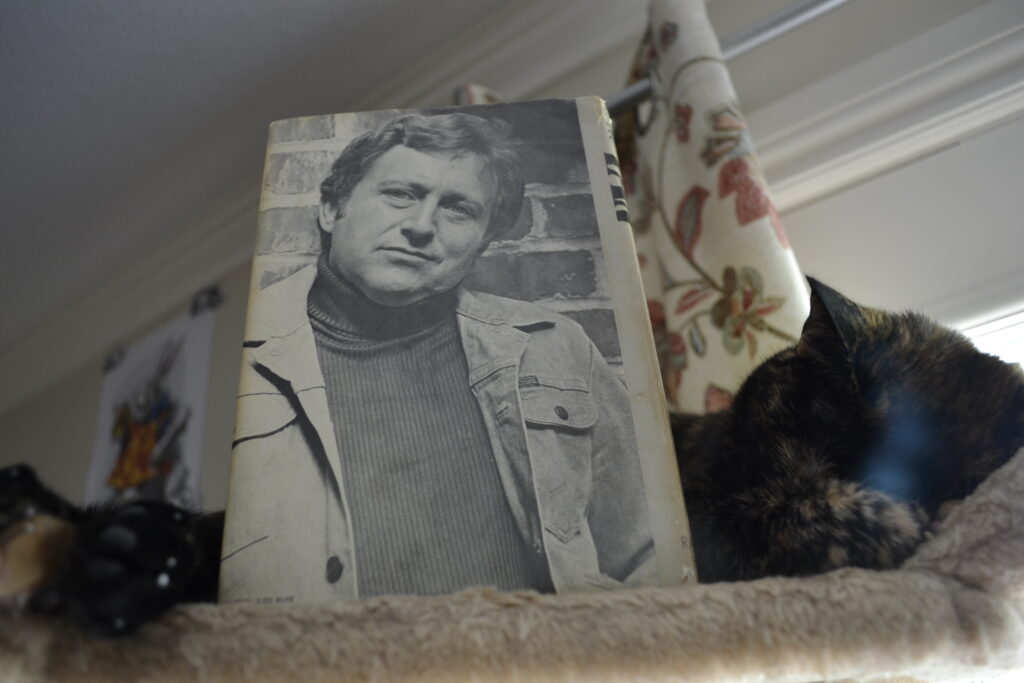 A tortoiseshell cat sleeps curled around The Fan, with Bob Randall on the back cover.