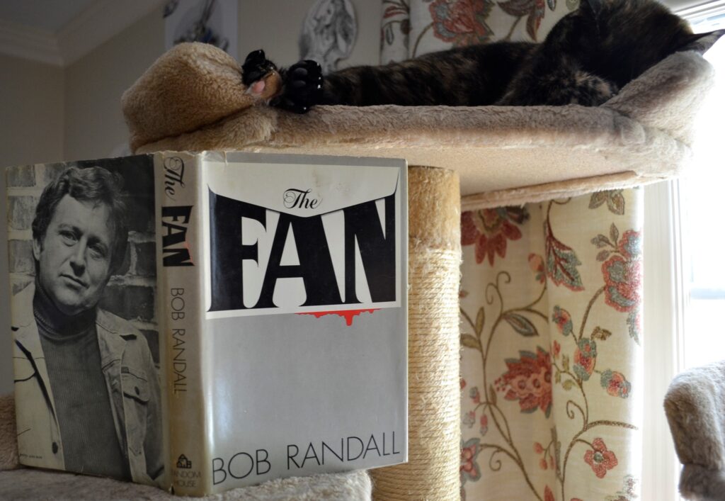 A tortoiseshell cat sleeps above the grey first edition of The Fan.