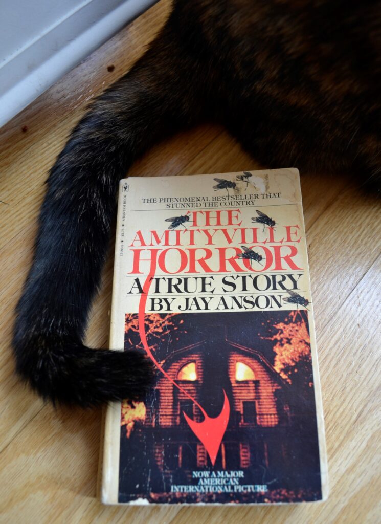 A dark tail curls around the demonic cover of The Amityville Horror.