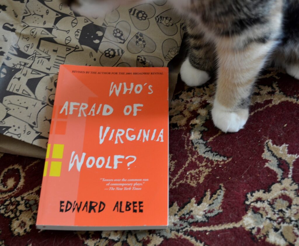 Two white paws with calico spots stand beside Who's Afraid of Virginia Woolf?