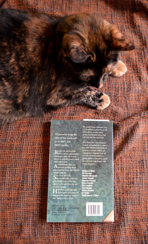 A tortoiseshell cat eyes the blue-green back cover of a book.