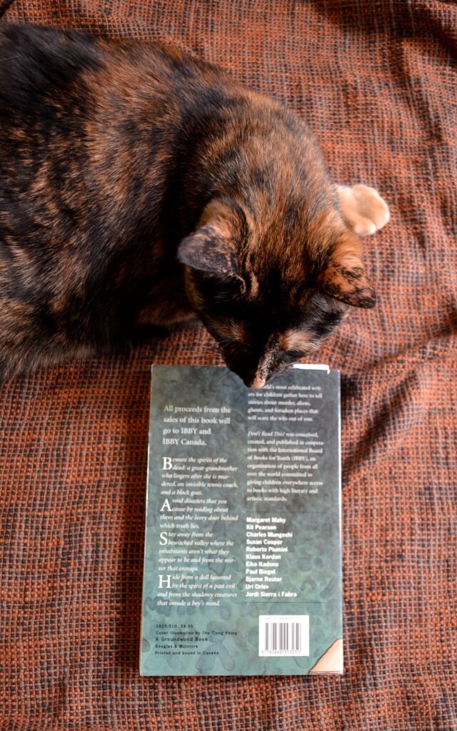 A tortoisteshell cat looks at the back cover of Don't Read This!