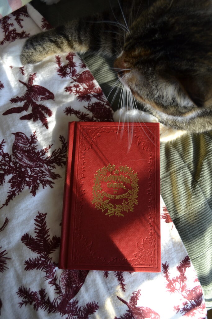 A red cover is heavily embossed with holly around a golden title that reads 'A Christmas Carol'.