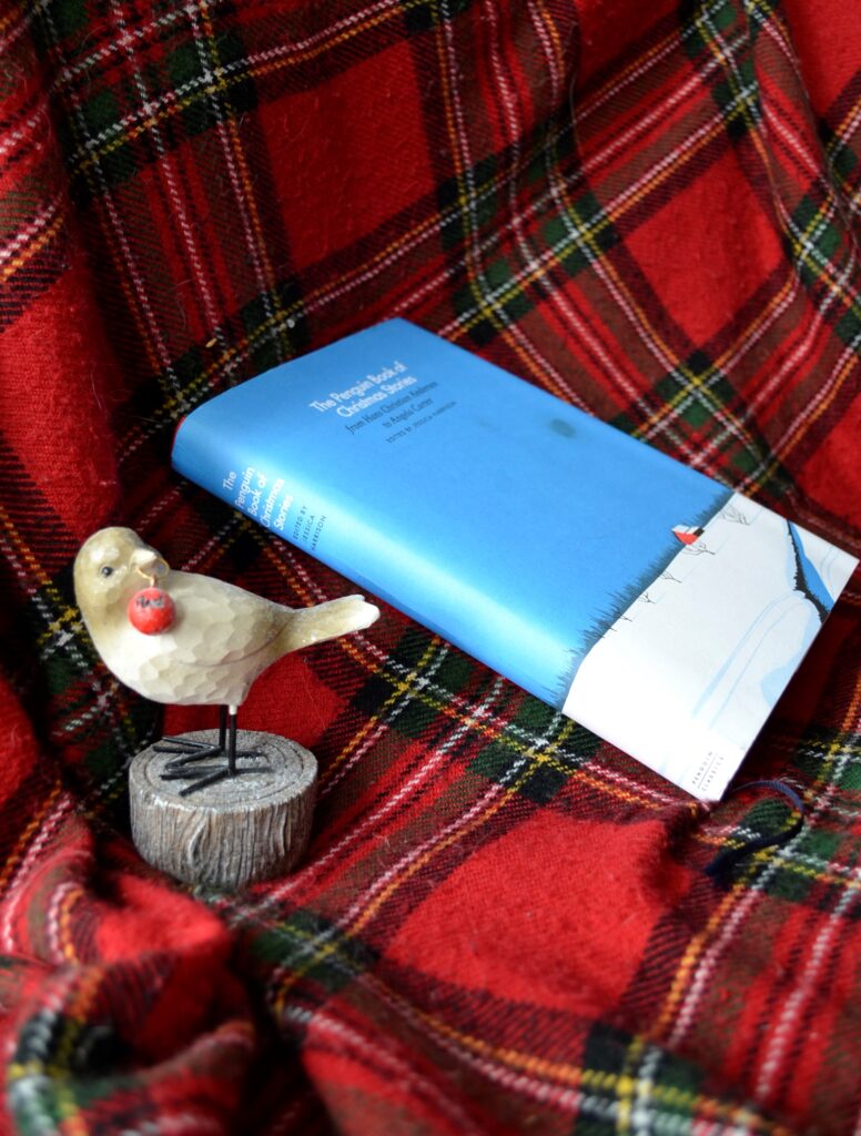 The blue and white cover of the Penguing Book of Christmas Stories sits beside a bird holding an ornament.