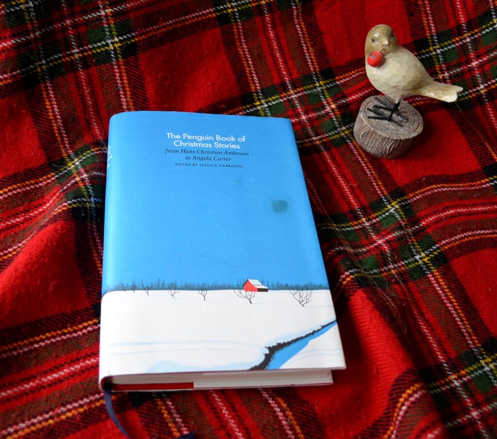 A book with a cover showing stark blue sky and snow sits on red tartan beside a statue bird.