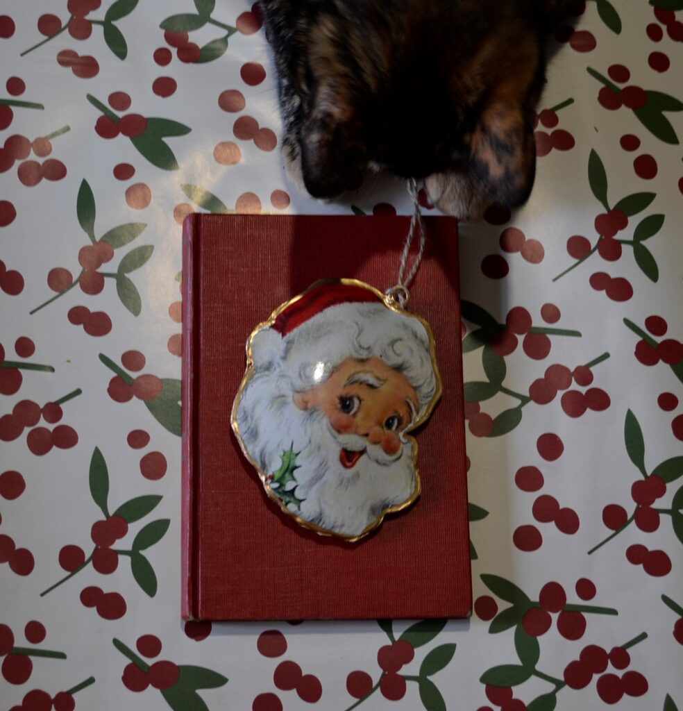 A tortoiseshell cat takes a Santa ornament from on top of Miracle on 34th Street.