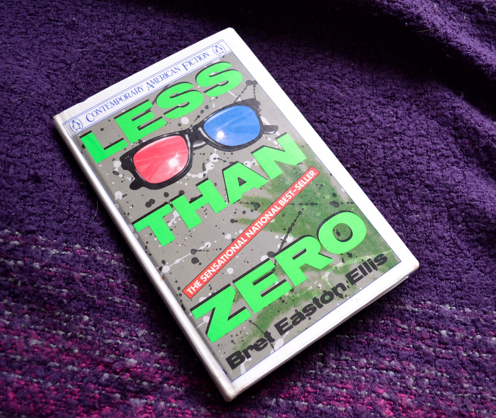 The title 'Less Than Zero' is visible on a book decorated with neon, splatter print, and 3-D glasses.
