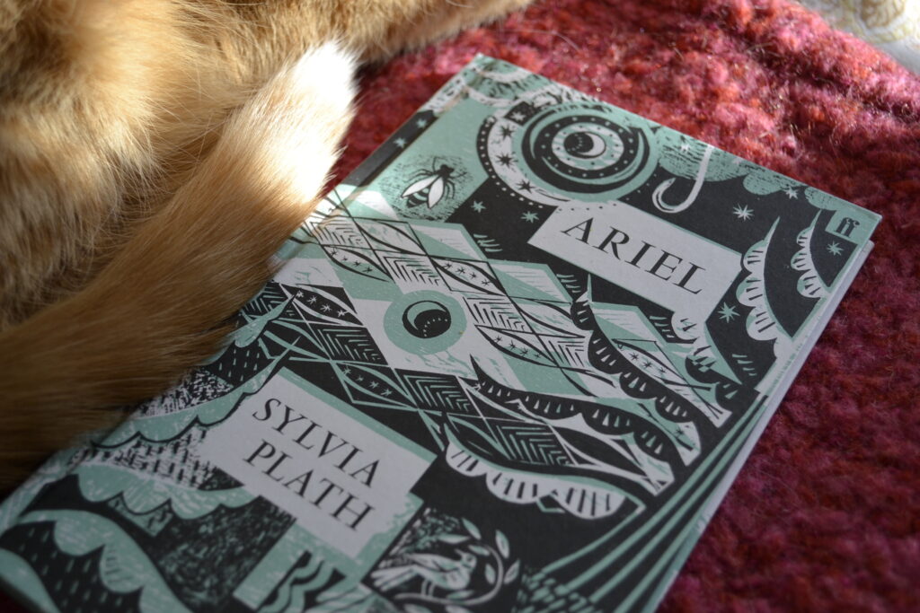 Ariel by Sylvia Plath. There are images of trees and water and bugs on the cover. An orange tail lies beside the book.