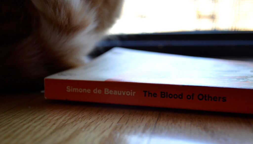 The orange spine of a book reads: Simone de Beauvoir The Blood of Others.