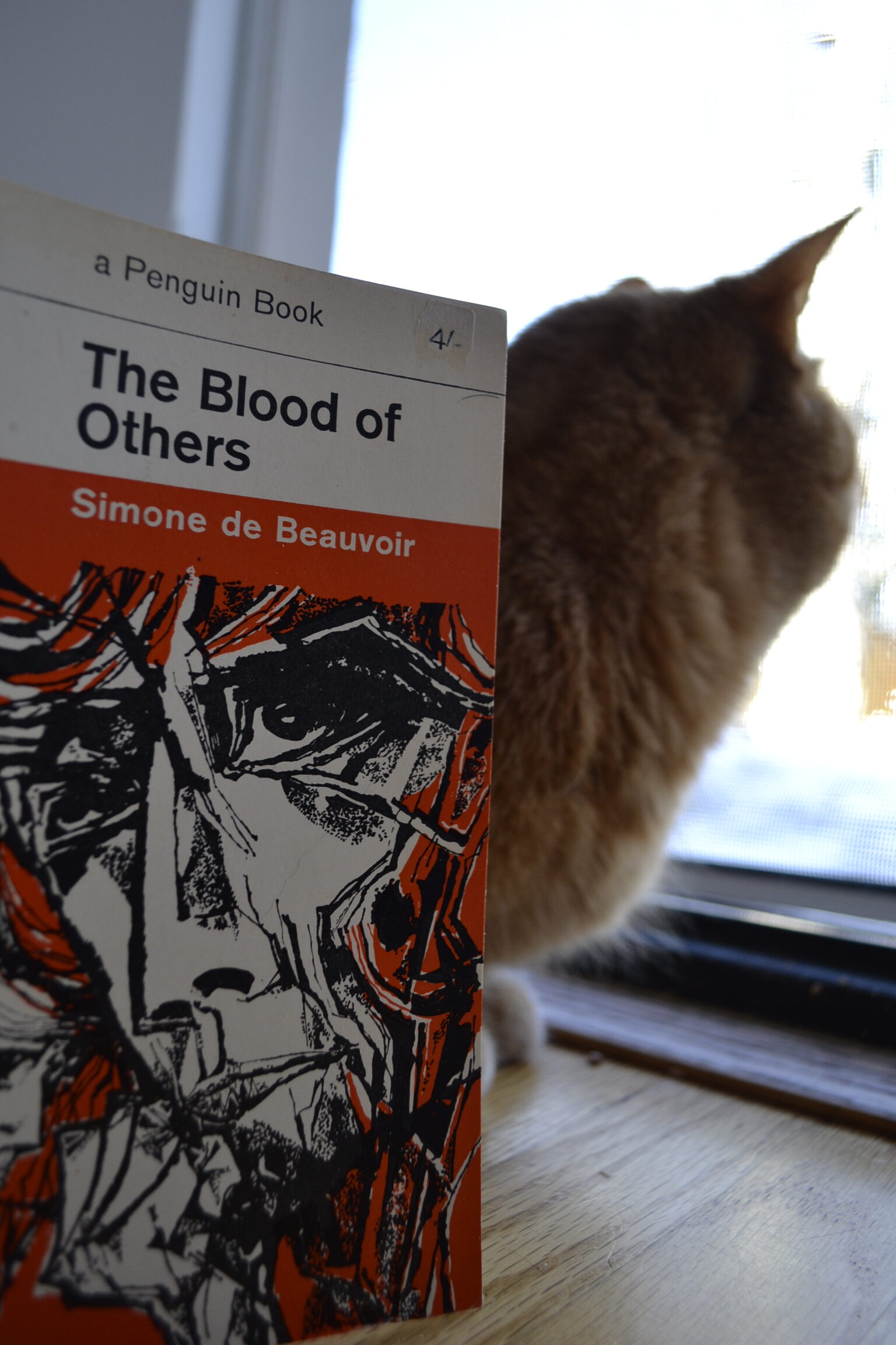 A jagged and scrambled image of a face on an orange book sits beneath the title: The Blood of Others.