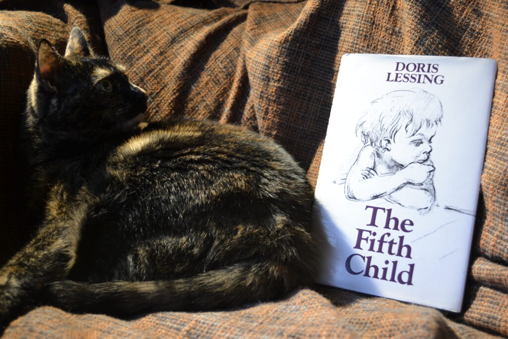 A tortoiseshell cat sits beside Doris Lessing's The Fifth Child.