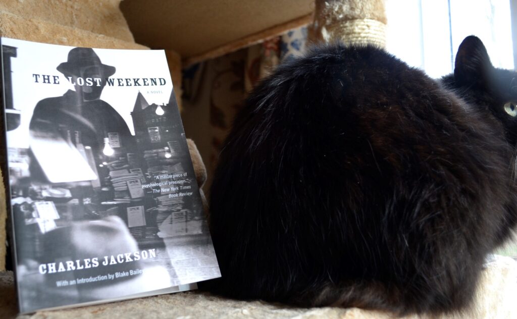 The Lost Weekend sits beside the black and fluffy tail of a cat.