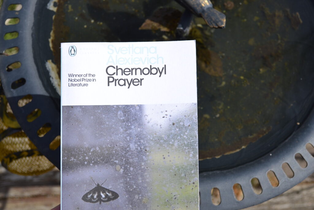 Above a birdbath full of algae, a white book reads 'Svetlana Alexievich' and 'Chernobyl Prayer'.