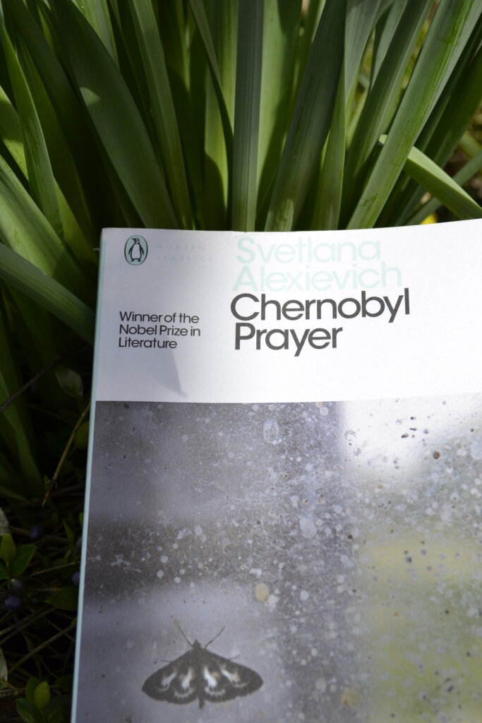 Resting against green fronds, a book cover reads 'Svetlana Alexievich Chernobyl Prayer'.