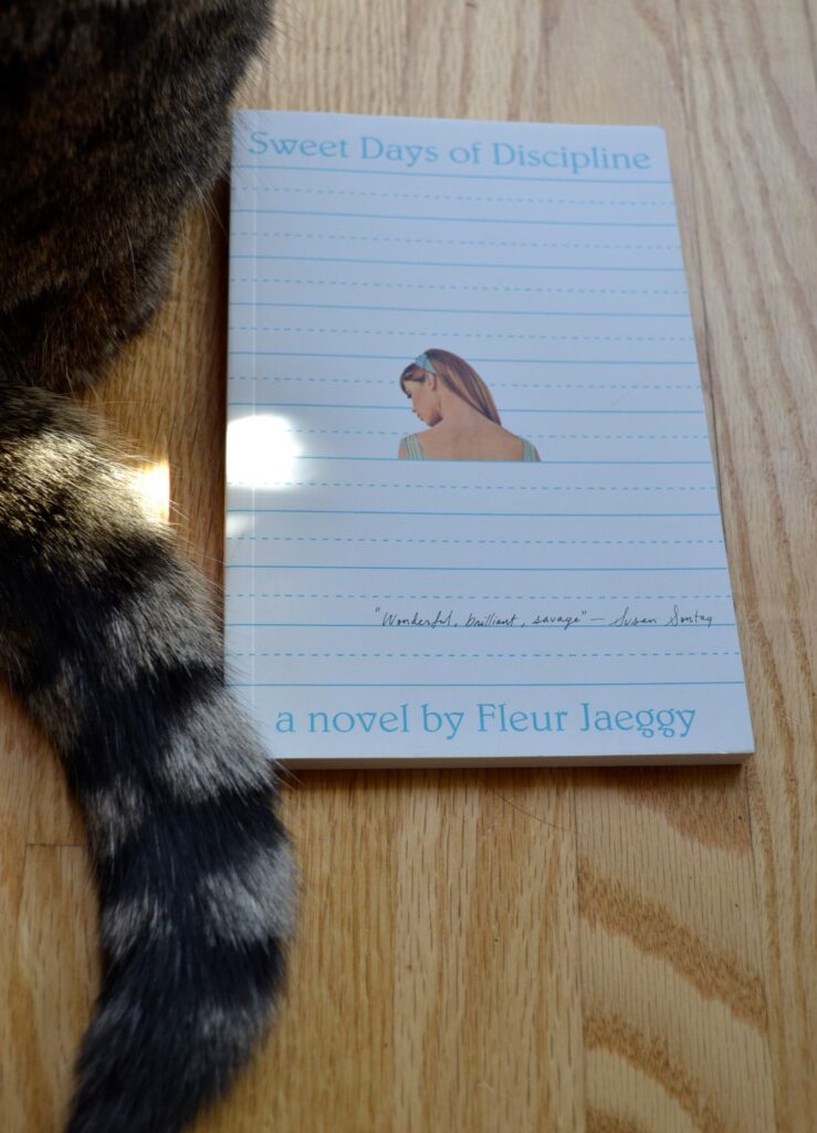 A striped tail curls around a book that is styled like lined paper with the back of a girl's neck featured in the centre.