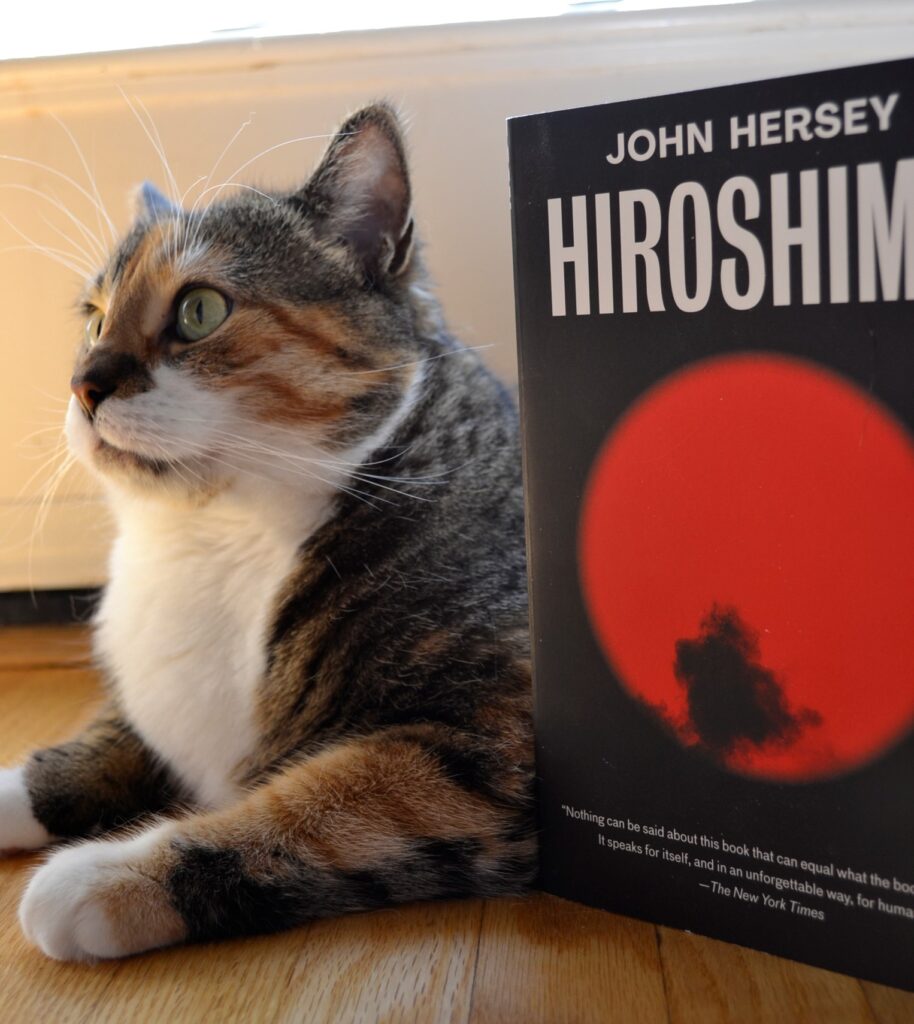 A calico tabby sits majestically beide John Hersey's Hiroshima.
