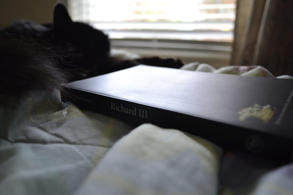 A black cat sleeps beside a black book titled Richard III.