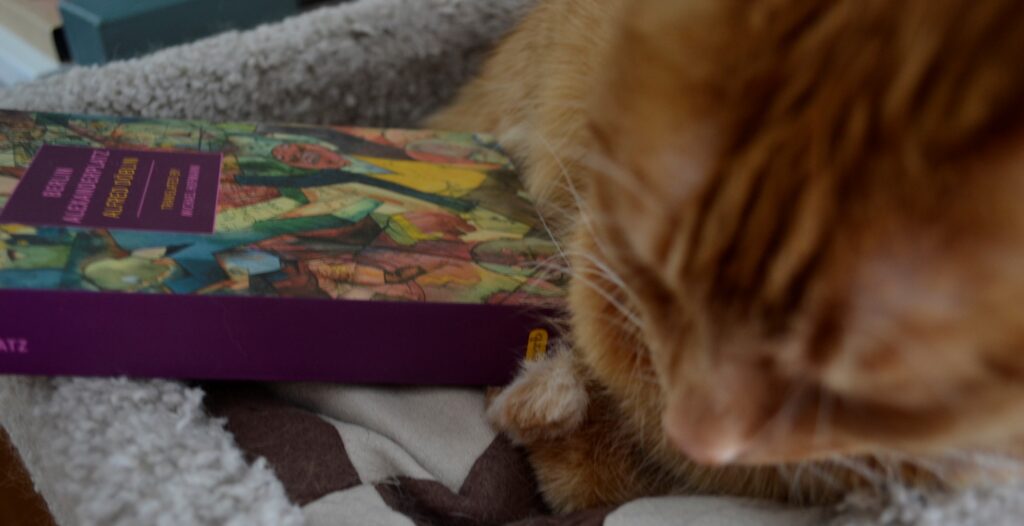 An orange cat curls around abook with a busy, geometric cover and a purple spine.