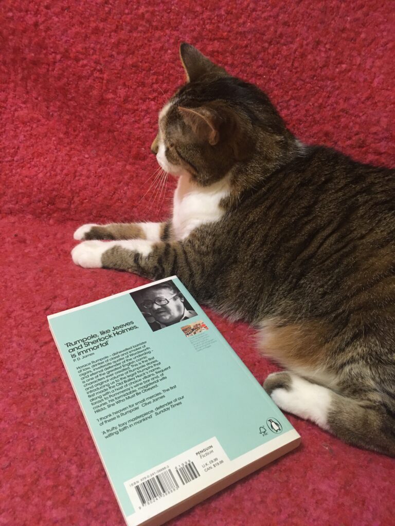 A tabby cat sits beside a copy of Rumpole of the Bailey.