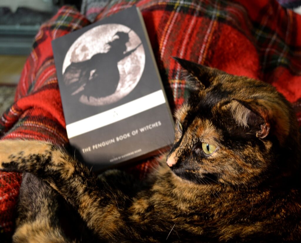 A tortoiseshell cat curls around The Penguin Book of Witches.