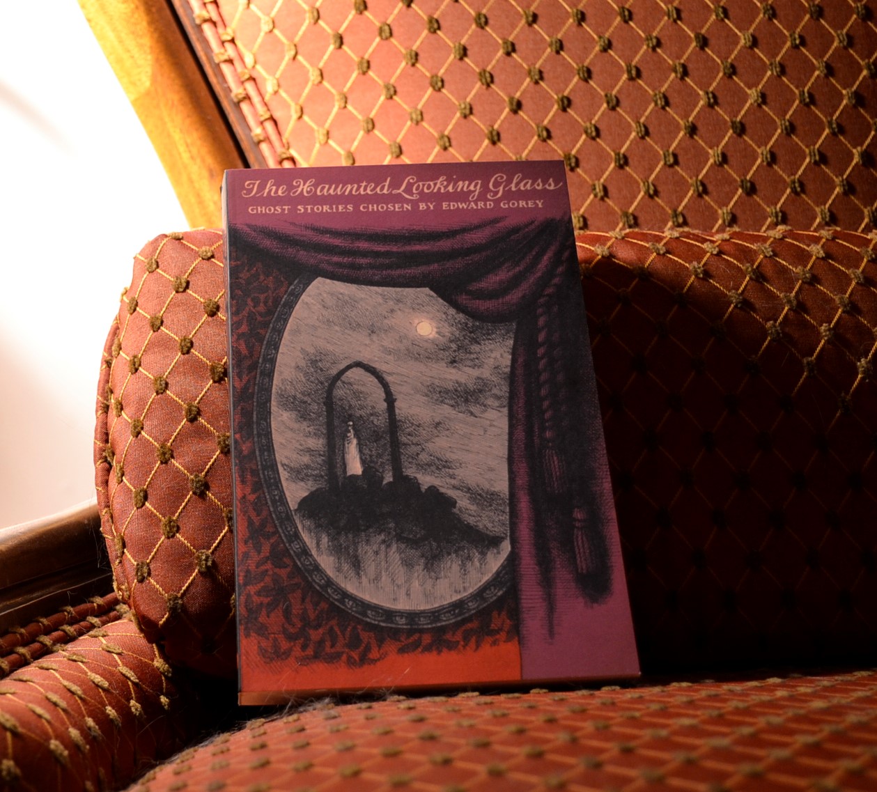 The cover of The Haunted Looking Glass shows a mirror behind a curtain reflecting a doorway on a hill.