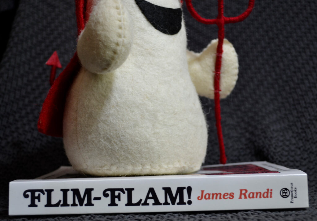 A white book spine reads Flim-Flam! The author is James Randi, and the publisher is Prometheus Books.