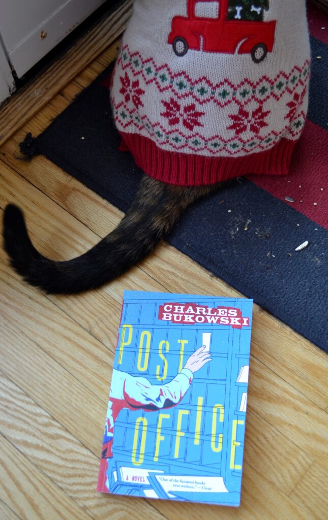 A copy of Post Office lies beside a cat. The cover shows a postal worker sorting mail.