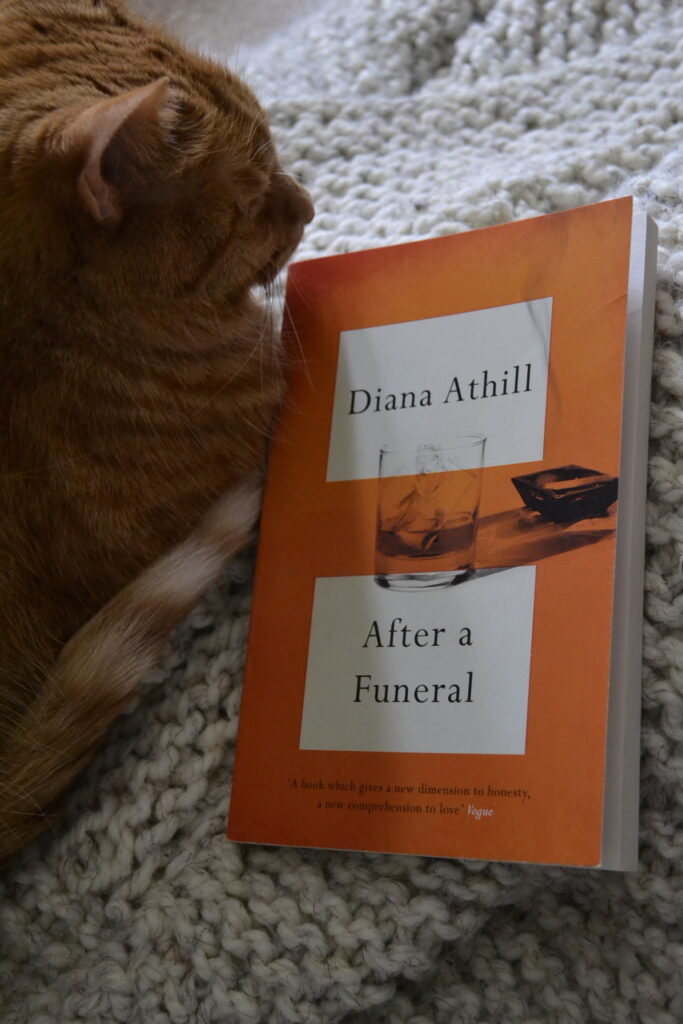 An orange cat sleep on a squishy white knitted blanket beside an orange book.