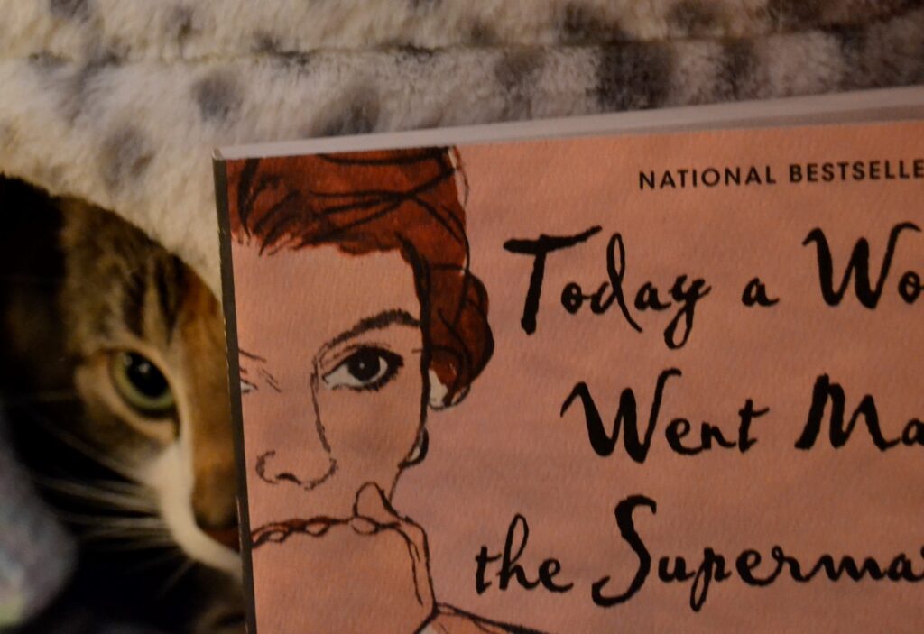 A cat lurks behind the edge of a book showing half a woman's face. The cat's half face completes the woman's face.