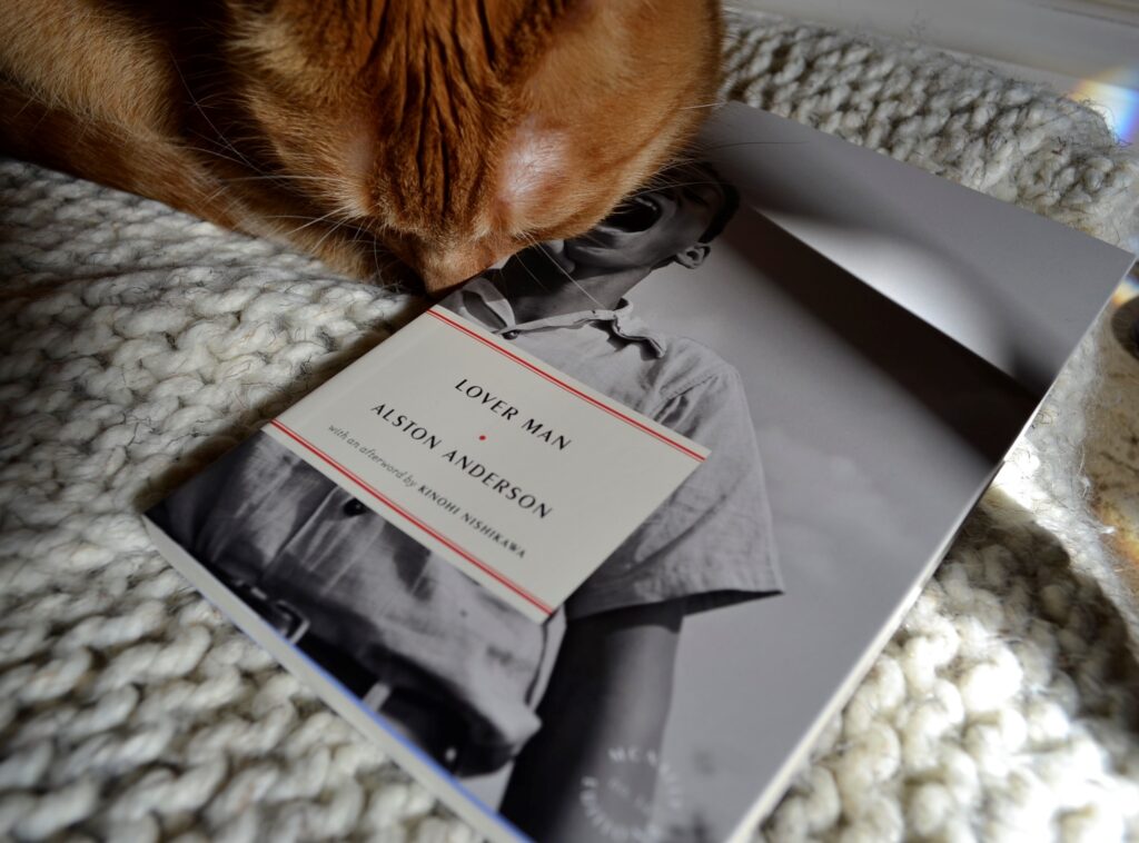 An orange cat nuzzles and black-and-white book. The book is Lover Man by Alston Anderson.