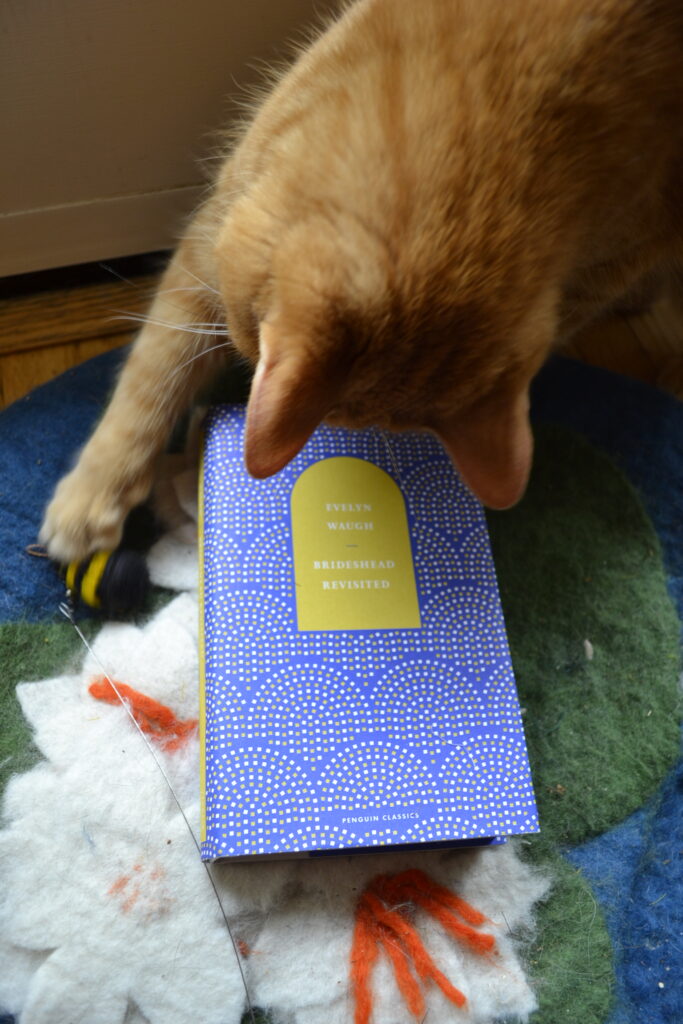 An orange cat paws a bee toy over Brideshead Revisited.