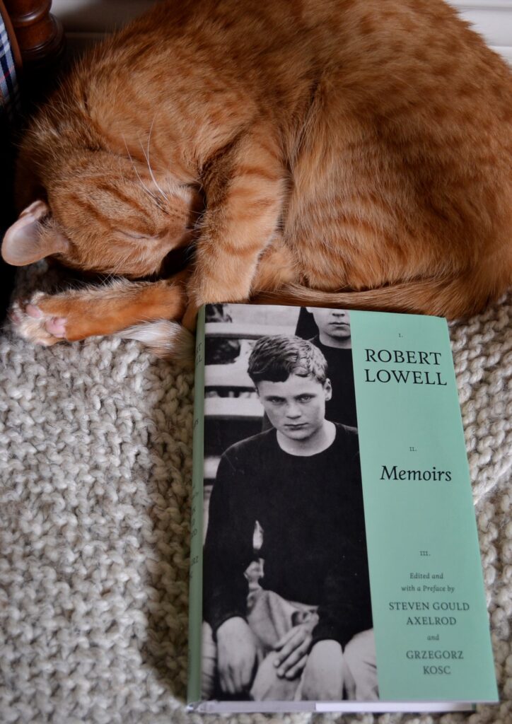 An orange cat sleeps sweetly beside Robert Lowell's Memoirs. The cover shows a glowering young boy on one side and a pale green bar with text on the other.