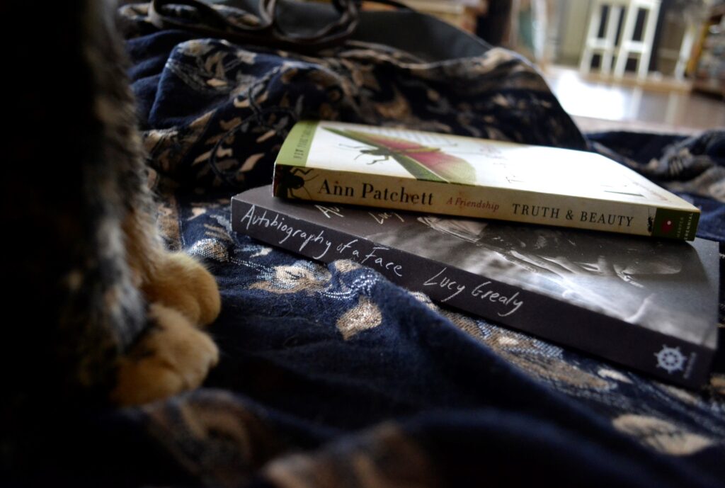 Ann Patchett's Truth & Beauty and Lucy Grealy's Autobiography of a Face lie stacked beside a pair of orange paws.