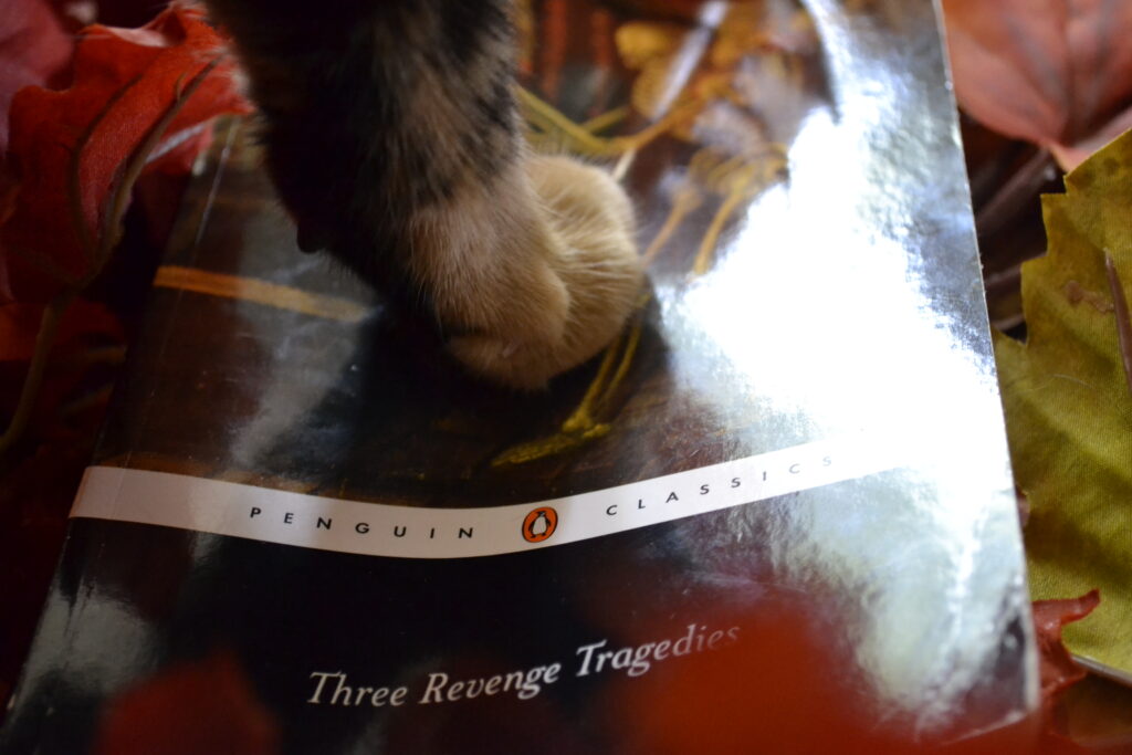 A black and orange paw steps firmly on a book — Three Revenge Tragedies, compiled by Penguin Classics.