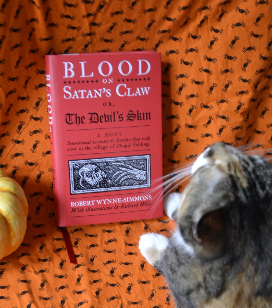 A red book with a lot of text and a woodcut drawing of a skull and oblong hand sit on a background.