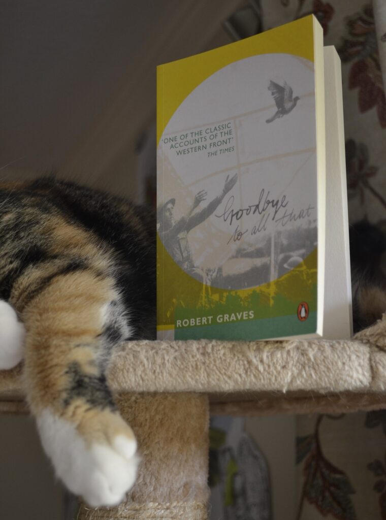 A copy of Goodbye to All That sits on the top of a cat tree, with a calico tabby lounging beside it.