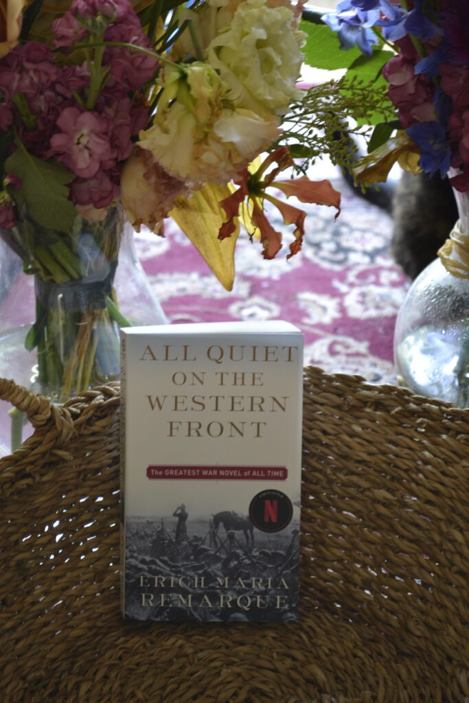 A copy of All Quiet on the Western Front by Erich Maria Remarque features a picture of a WWI battlefield full of sandbags and dead bodies.